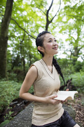 Junge Frau hält ein Buch im Wald. - MINF02596