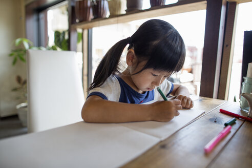 Mädchen mit Zöpfen sitzt an einem Tisch und zeichnet mit Filzstiften. - MINF02621