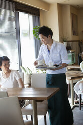 Kellner bedient eine Frau, die an einem Tisch in einem Café sitzt. - MINF02624