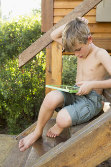 Ein Junge sitzt draußen und spielt auf seinem digitalen Tablet. - MINF02633