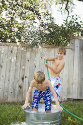 Zwei Brüder spielen in einem Garten mit einer mit Wasser gefüllten Wanne und einem Schlauch. - MINF02640