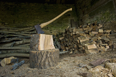 Eine Axt, die in einem Stück Holz auf einem Hackklotz steckt, ein Haufen Holzstämme und gehacktes Holz. - MINF02651