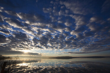 A dramatic cloud pattern across the sky and the sun setting over the waters of a lake. - MINF02668