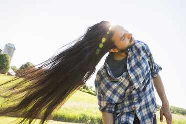 A young man letting down his very long dark hair and shaking his head to fan it out in the fresh air. - MINF02709