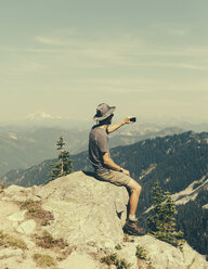 Ein Wanderer auf einem Berggipfel, der sein Smartphone in der Hand hält, auf dem Gipfel des Surprise Mountain in der Alpine Lakes Wilderness im Mount Baker-Snoqualmie National Forest. - MINF02721