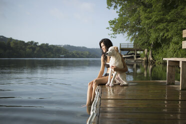 Eine Frau, die ihren Arm um einen kleinen weißen Hund auf einem Steg an einem See legt. - MINF02736