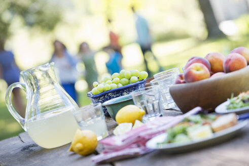 Ein sommerliches Buffet mit Obst und Gemüse, das auf einem Tisch angerichtet ist, mit Menschen im Hintergrund. - MINF02763