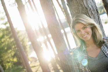 A woman standing in the shadows of tall trees on the shores of a lake in summer. - MINF02766