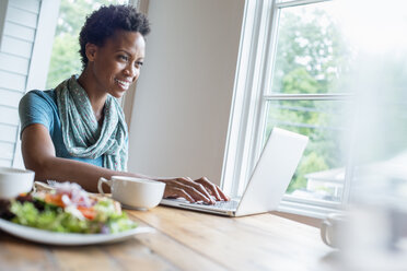 Eine Frau sitzt in einem Café mit einer Tasse Kaffee und einer Mahlzeit und benutzt einen Laptop. - MINF02767