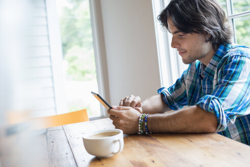 Ein Mann sitzt mit einer Tasse Kaffee in einem Café und benutzt ein digitales Tablet. - MINF02768