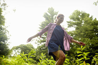 A woman walking through the undergrowth in woodland, with her arms brushing the tops of the wild plants. - MINF02774