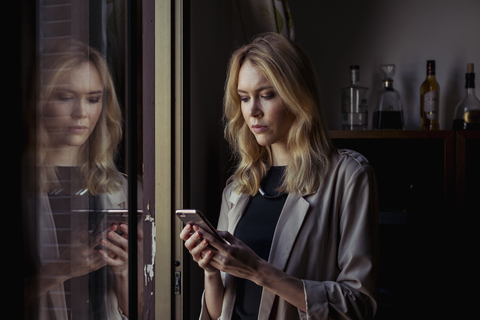 Porträt einer blonden jungen Frau, die auf ihr Mobiltelefon schaut, lizenzfreies Stockfoto