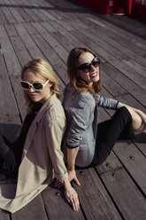 Porträt von zwei modischen jungen Frauen mit Sonnenbrillen, die auf einem Holzboden sitzen - MAUF01528