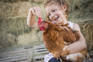 Ein junges Mädchen hält ein Huhn in einem Hühnerstall. - MINF02815