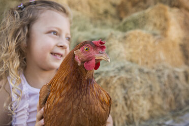 A young girl holding a chicken in a henhouse. - MINF02816