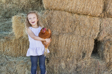 Ein junges Mädchen steht in einem Heustall und hält ein Huhn im Arm. - MINF02818