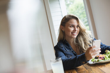 A young woman using a smart phone, seated at a table. Coffee and a sandwich. - MINF02852