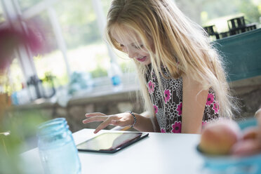 Ein junges Mädchen in einem geblümten Kleid sitzt an einem Tisch und benutzt ein digitales Tablet. - MINF02855