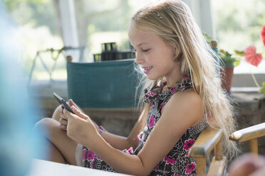 A young girl in a flowered dress using a digital tablet. Sitting at a table. - MINF02856