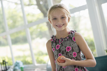 Ein junges Mädchen in einem geblümten Kleid hält eine Pfirsichfrucht. - MINF02861
