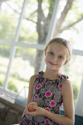 A young girl in a floral dress holding a peach fruit. - MINF02862