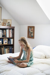 A young girl sitting on her bed using a digital tablet. - MINF02868