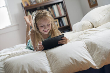 Ein junges Mädchen sitzt auf ihrem Bett und benutzt ein digitales Tablet. - MINF02869