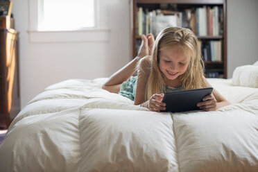 Ein junges Mädchen sitzt auf ihrem Bett und benutzt ein digitales Tablet. - MINF02870