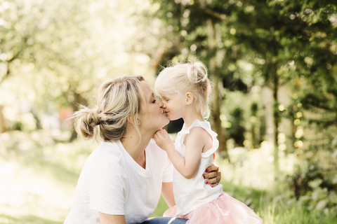 Glückliche Mutter küsst ihre kleine Tochter im Freien, lizenzfreies Stockfoto