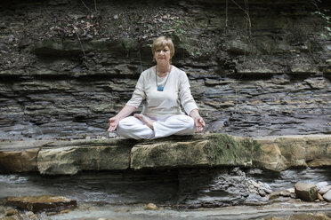 Senior woman doing yoga, meditating on rock - ALBF00583