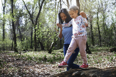 Mother and daughter in park, girl balancing on tree trunk - AZF00013