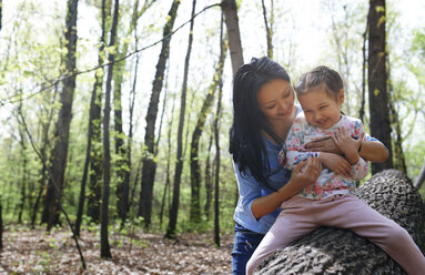 Mother and daughter in park, sitting on tree trunk - AZF00031