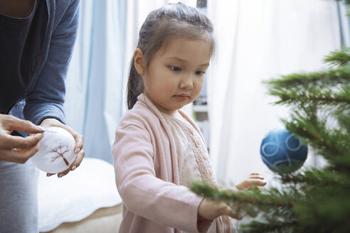 Porträt eines kleinen Mädchens beim Schmücken des Weihnachtsbaums mit ihrer Mutter - AZF00037
