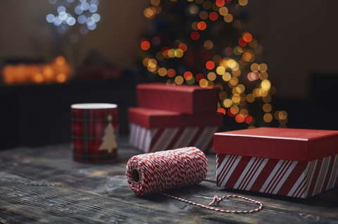 Eine Rolle rot-weißes Packgarn und Geschenkkartons vor einem beleuchteten Weihnachtsbaum, lizenzfreies Stockfoto