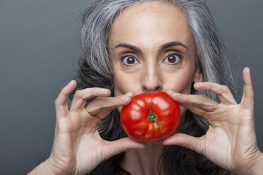 Reife Frau bedeckt Mund mit roter Tomate - ISF17159