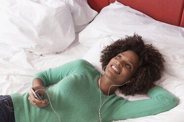 Woman listening to earphones on bed - ISF17201