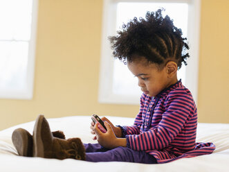 Mädchen spielt mit Handy auf dem Bett - ISF17301