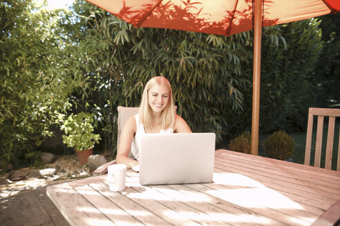 Junge Frau benutzt Laptop im Garten - KMKF00401