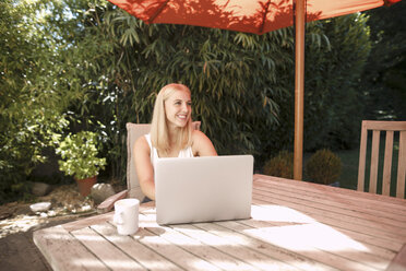 Junge Frau benutzt Laptop im Garten - KMKF00402