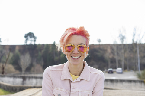Porträt einer jungen lachenden Frau, Sonnenbrille und rosa Jeansjacke, lizenzfreies Stockfoto