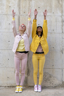 Two alternative friends wearing yellow and pink jeans clothes, posing, raising arms - AFVF01045