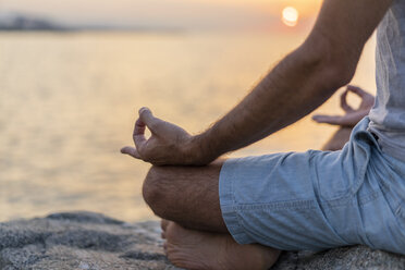 Spanien: Mann meditiert bei Sonnenaufgang am felsigen Strand, Mudra - AFVF01062