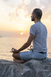 Spain. Man meditating during sunrise on rocky beach - AFVF01063