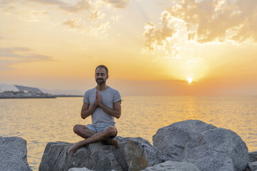 Spain. Man meditating during sunrise on rocky beach - AFVF01065