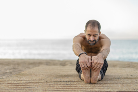Spanien: Ein Mann macht abends am Strand Yoga und dehnt die Beine, lizenzfreies Stockfoto