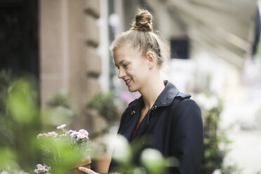 Lächelnde junge Frau bei der Auswahl einer Topfpflanze vor einem Blumenladen - SGF02198