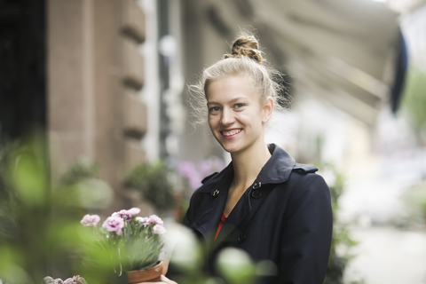 Porträt einer lächelnden jungen Frau, die eine Topfpflanze vor einem Blumenladen auswählt, lizenzfreies Stockfoto