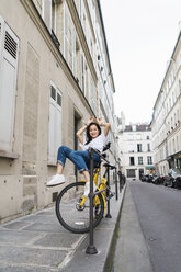 Verspielte junge Frau auf dem Fahrrad am Straßenrand - AFVF01091