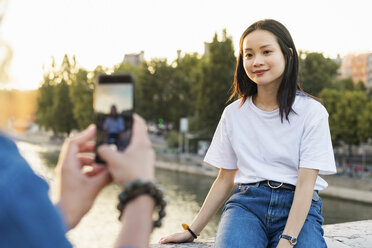 France, Paris, man taking a picture of his girlfriend at river Seine at sunset - AFVF01123