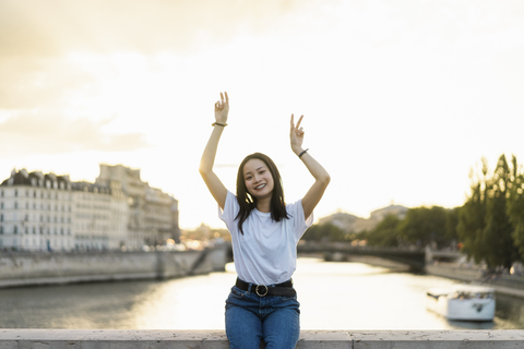 Frankreich, Paris, Porträt einer glücklichen jungen Frau am Fluss Seine bei Sonnenuntergang, lizenzfreies Stockfoto